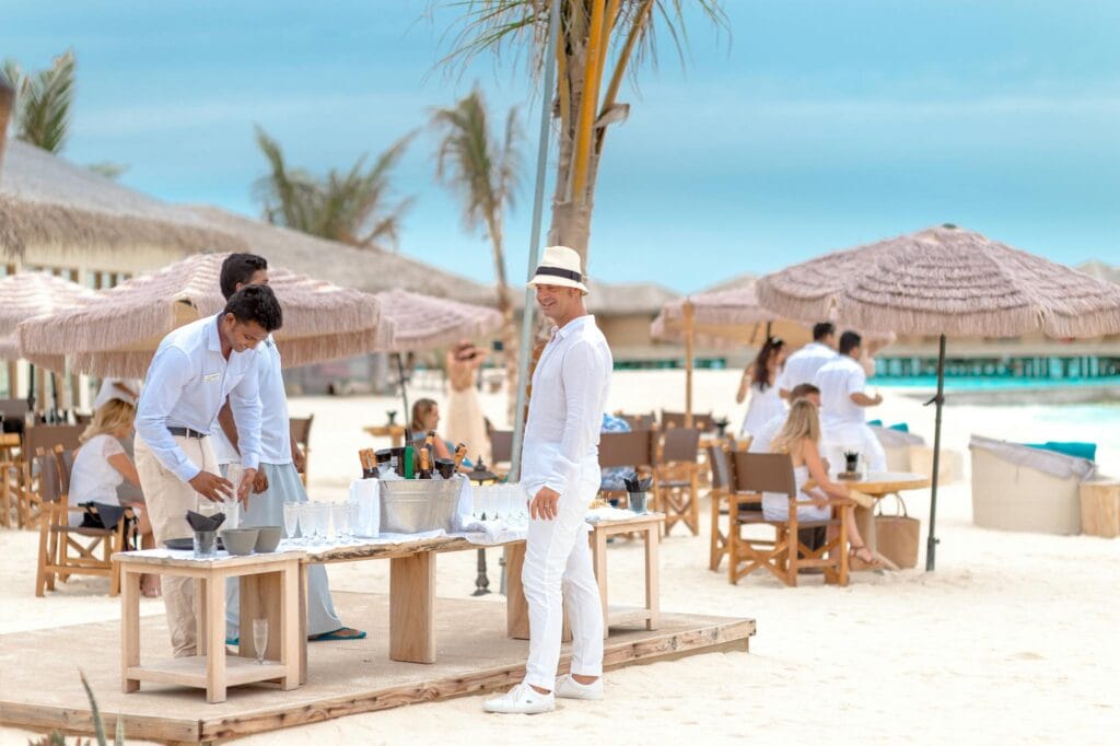 Sophisticated beach party setup with guests in white enjoying a sunny day by the ocean.